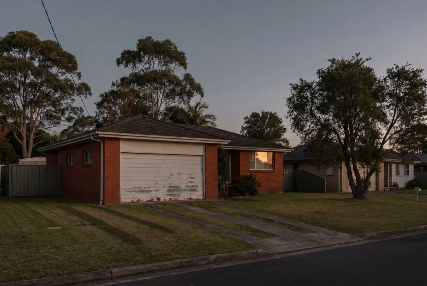 A single-storey brick house on a flat street with an original garage door weathered along its bottom edge