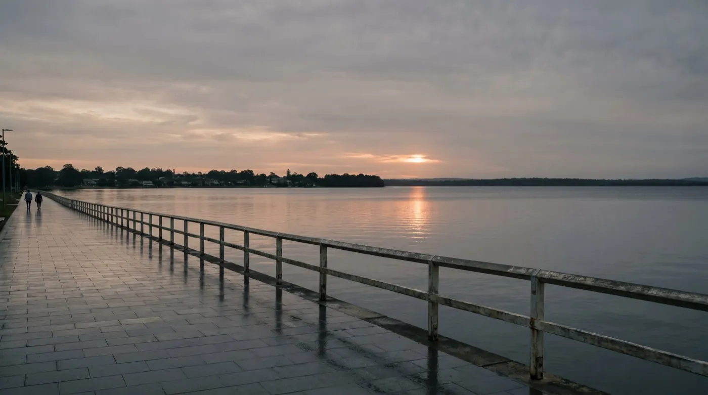 The Warners Bay foreshore promenade at evening, with the lake stretching to a level horizon and the low sun laying a copper path on the water